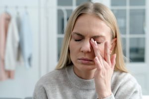 Frau mit geschlossenen Augen reibt sich das Auge aufgrund von Trockenheit oder Reizung – Symbolbild für trockene Augen und natürliche Linderung durch Omega-3, CBD-Öl und pflanzliche Wirkstoffe.