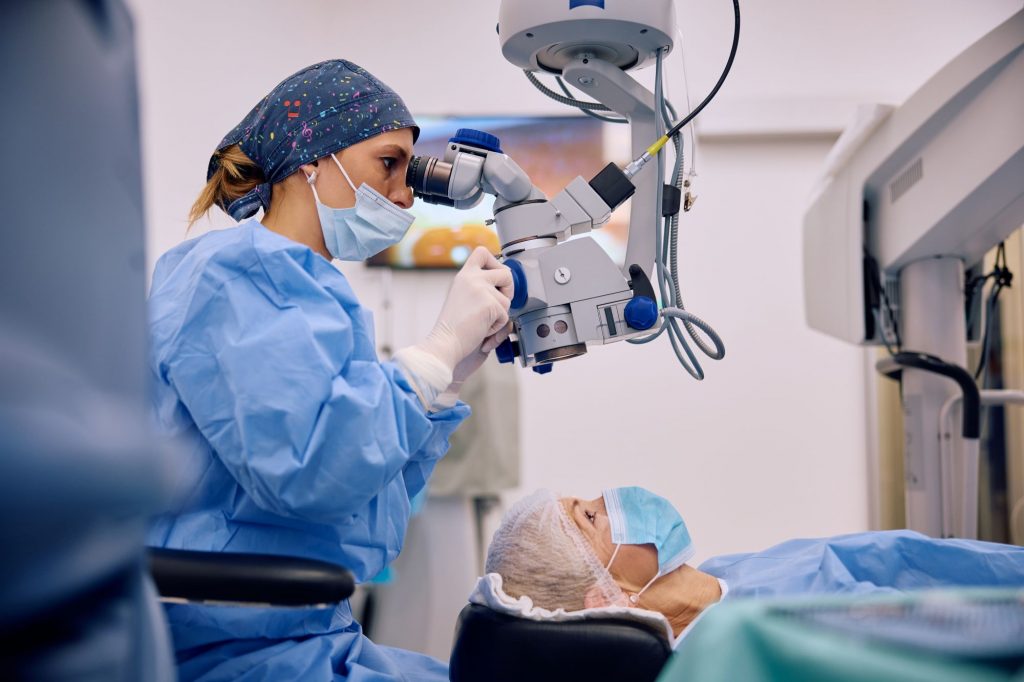 Augenoperation mit Operationsmikroskop: Chirurgin behandelt Patientin im OP, vermutlich minimalinvasive refraktive Laserbehandlung (z. B. SMILE-Methode) zur Korrektur von Fehlsichtigkeit.